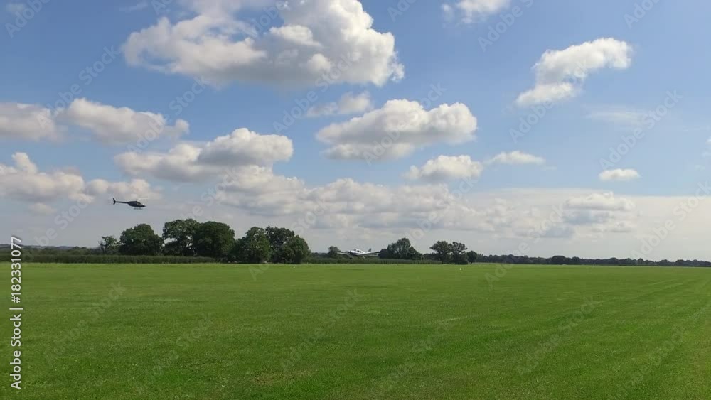 A Small Sport Plane Landing On A Green Field Off And Helicopter On The Field A Small Sport Plane Landing On A Green Field Off And Helicopter On The Field