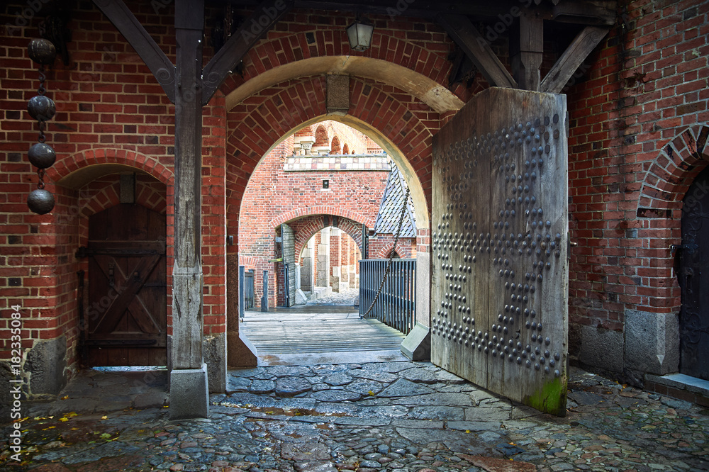 Fototapeta premium Gate in Castle of the Teutonic Order in Malbork, Poland. Red brick wall and cobblestone.