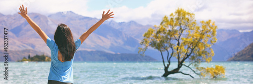Happy wellness freedom woman in New Zealand winning with arms up in success at Wanaka Lone Tree  popular travel destination. Happiness in life concept. Panoramic banner of joyful girl.