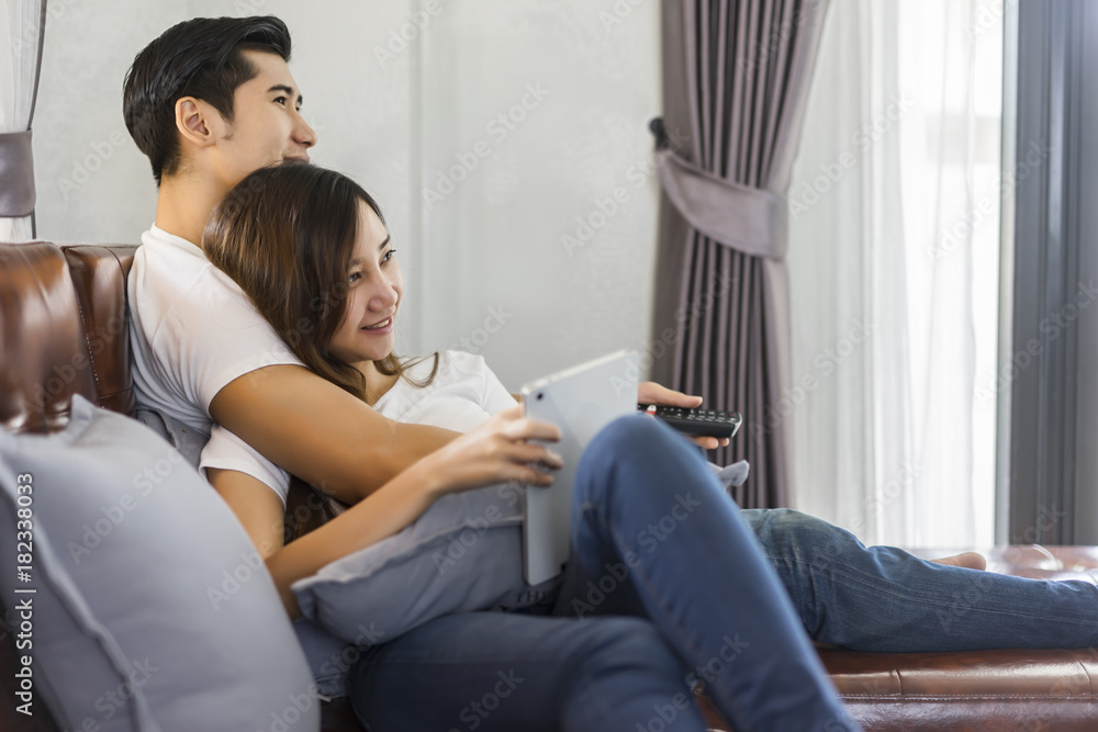 Obraz premium Young couple in love sitting on a brown sofa and watching television.