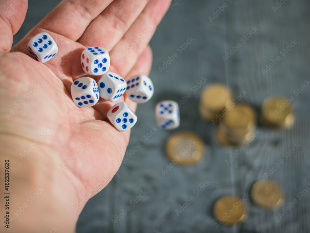 The man throws the game dice on the table with coins. Money and game cubes.