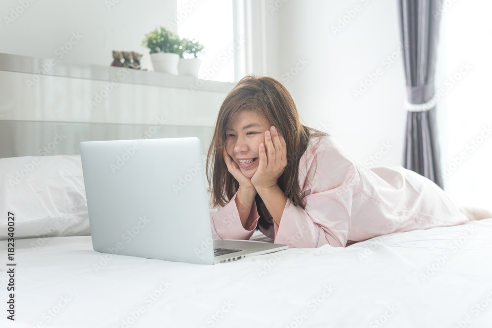 Happy woman relaxes on bed with a laptop computer in the morning Happy woman relaxes on bed with a laptop computer in the morning