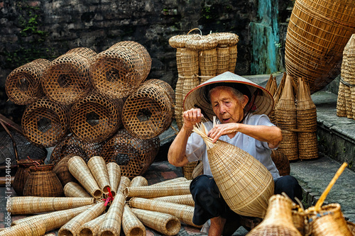 Old Vietnamese female craftsman making the traditional bamboo fish trap or weave at the old traditional house in Thu sy trade village, Hung Yen, Vietnam, traditional artist concept