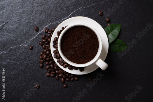 Coffee beans and powder coffee in the cup with leaves on the black stone.