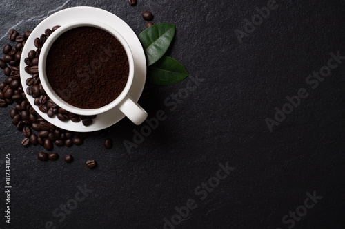 Coffee beans and powder coffee in the cup with leaves on the black stone.Top view with copy space.