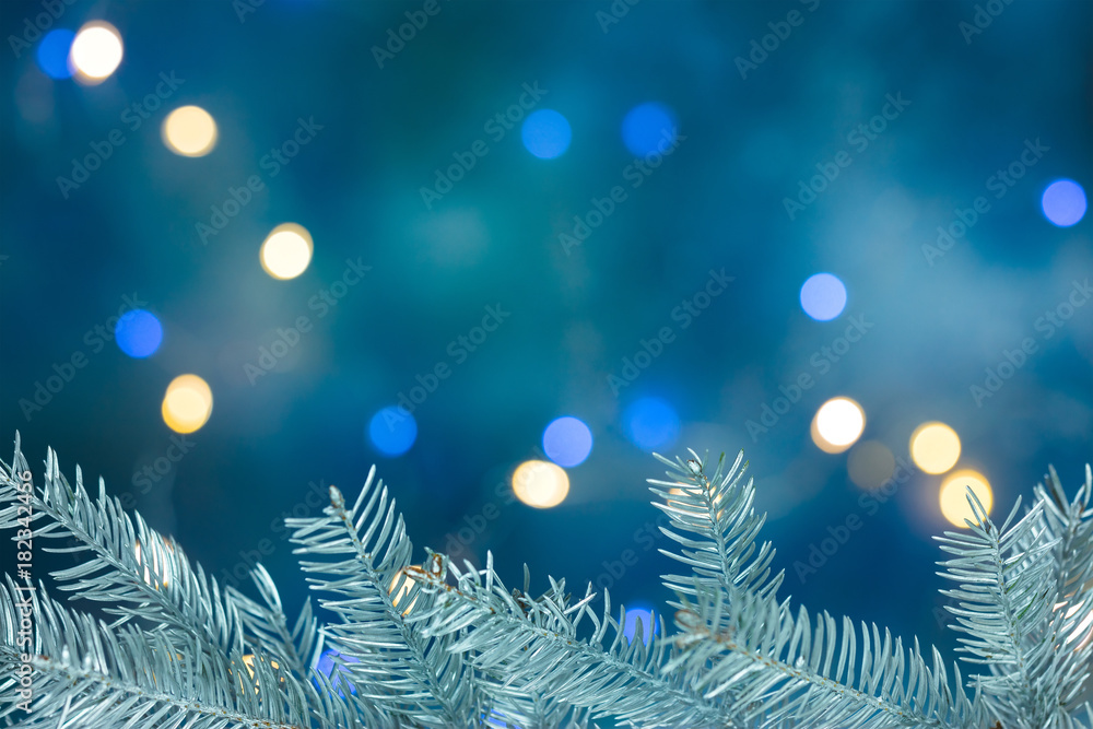 silver christmas tree branch on blurred blue background with holiday lights