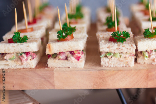 Canape  sandwiches with toothpicks and fresh vegetables on wooden board
