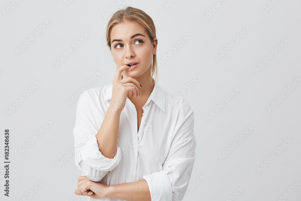 Studio shot of cunning beautiful woman with straight blonde hair looking aside holding hand under chin intending to realize tricky plan. Studio shot of cunning beautiful woman with straight blonde hair looking aside holding hand under chin intending to realize tricky plan.