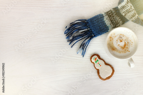 winter coffee break with mood/ white mug with cappuccino in blue scarf and ginger snowman on table top view