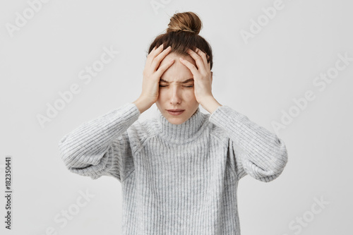 Exhausted young woman touching her head with eyes closed. Female exchange worker suffering from unbearable headache. Health concept