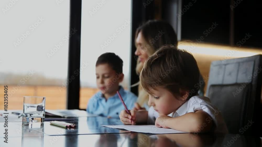 Happy family mother of two children helps the sons to do their homework sitting at the big table in the kitchen. Happy family mother of two children helps the sons to do their homework sitting at the big table in the kitchen.