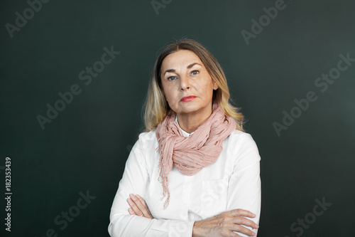 Canvas-taulu Blonde mature woman with skeptical strict expression on her wrinkled face, posing in studio, keeping arms folded, expressing suspicion or disapproval