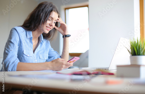 Beautiful young business woman sitting at office desk and talking on cell phone. Business woman