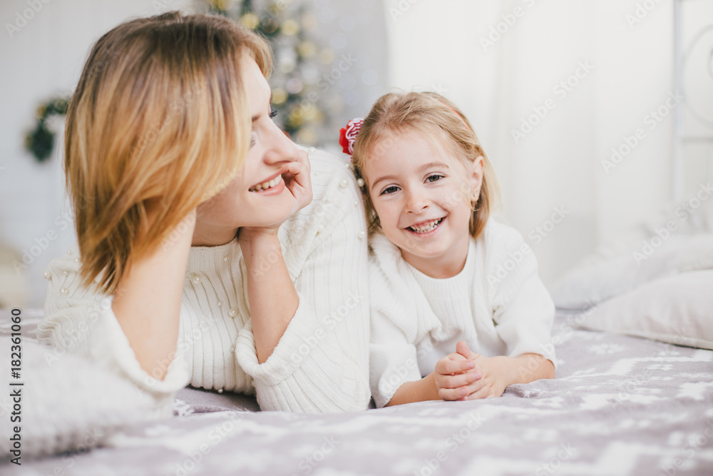 Happy beautiful mother and her little daughter posing near Christmas tree in a holiday interior Happy beautiful mother and her little daughter posing near Christmas tree in a holiday interior