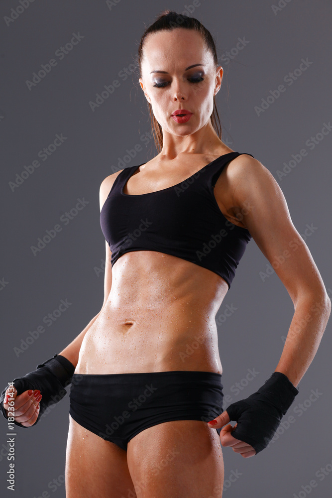 Obraz premium Muscular young woman standing on gray background. Muscular young woman