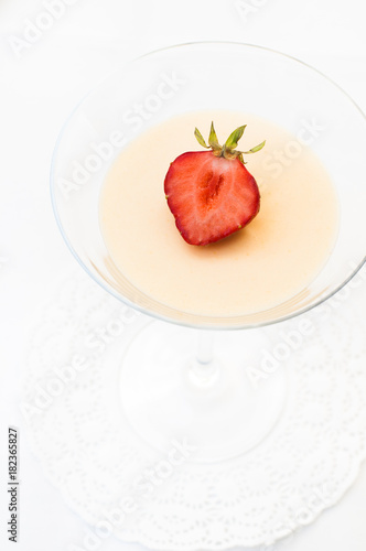 Creamy traditional Italian jelly dessert called Panna Cotta which is made of heavy cream, milk, vanilla and gelatin served in a cocktail glass and decorated with a strawberry on white table