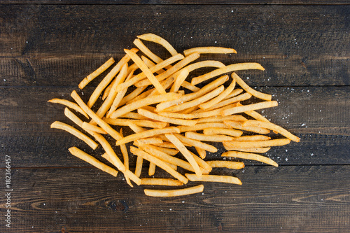 Potato fries with salt and pepper on the brown wooden background