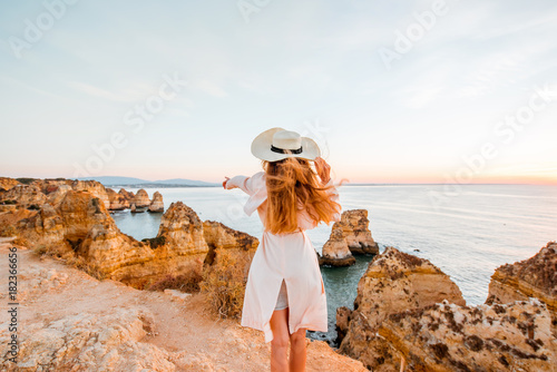 Woman enjoying great view on the rocky coastline during the sunrise in Lagos on the south of Portugal
