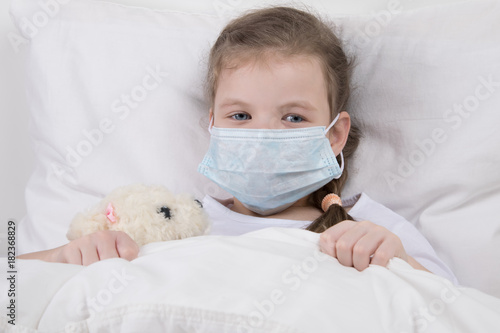 child in white bed, on his face is wearing a medical mask, against the flu