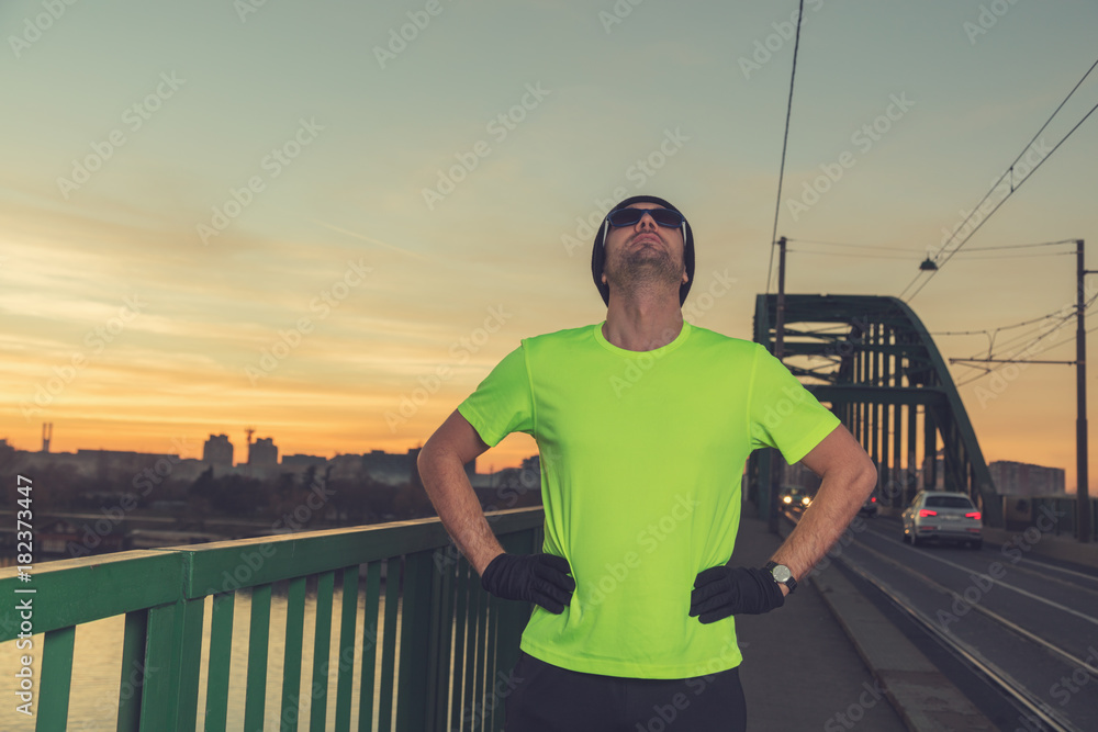 Urban jogger stretching on a bridge above the river in sunset / sunrise time.