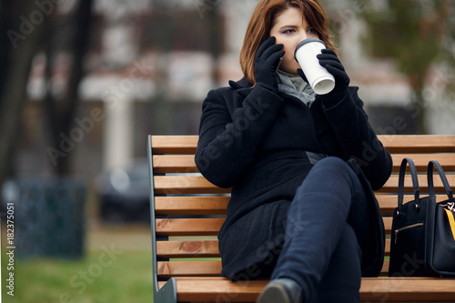 Picture of girl in black coat talking on phone and drinking coffee