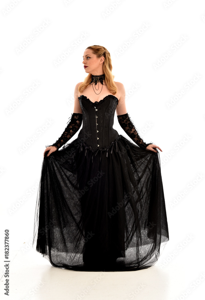 full length portrait of a blonde girl wearing black gothic gown. standing pose, isolated on white background.