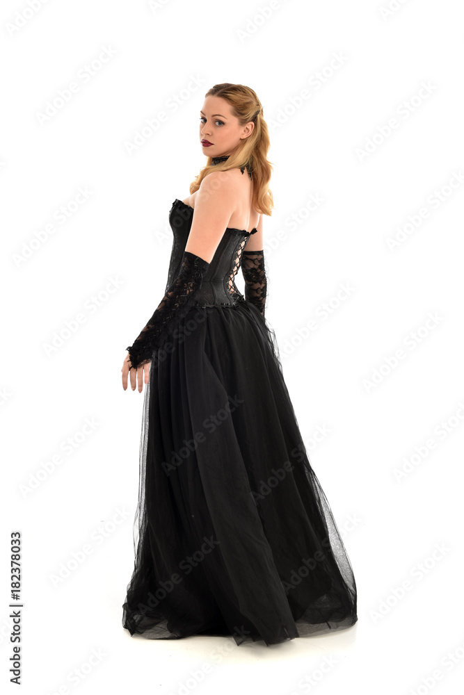 full length portrait of a blonde girl wearing black gothic gown. standing pose, isolated on white background.