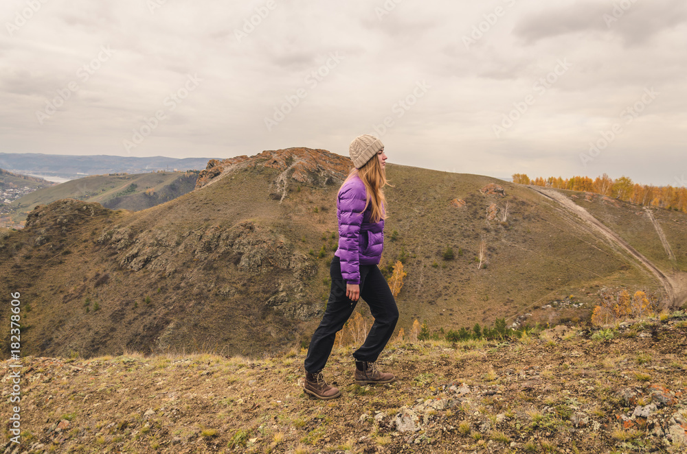 A girl in a lilac jacket walks in the mountains, an autumn forest with a cloudy dayю. Free space for text