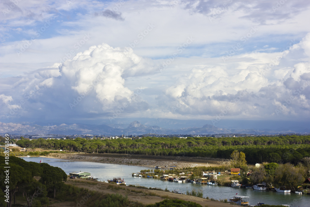 Landscape with a river and mountains. Large white cumulus clouds and purple clouds.