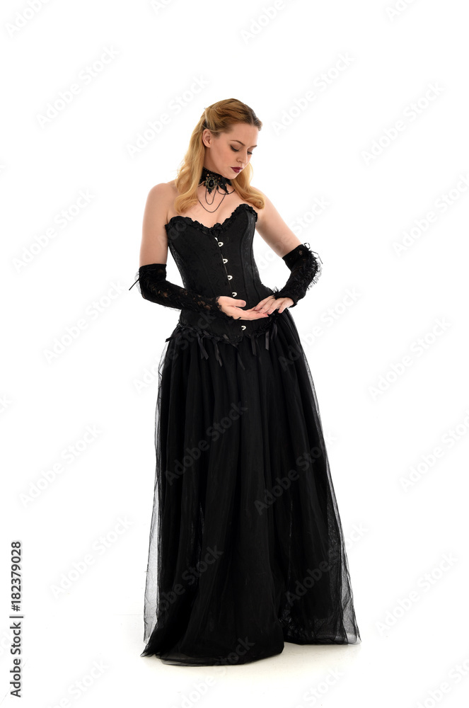 full length portrait of a blonde girl wearing black gothic gown. standing pose, isolated on white background.