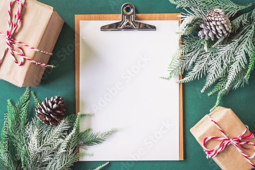 Blank paper with gift boxes and Christmas tree branches on green background.