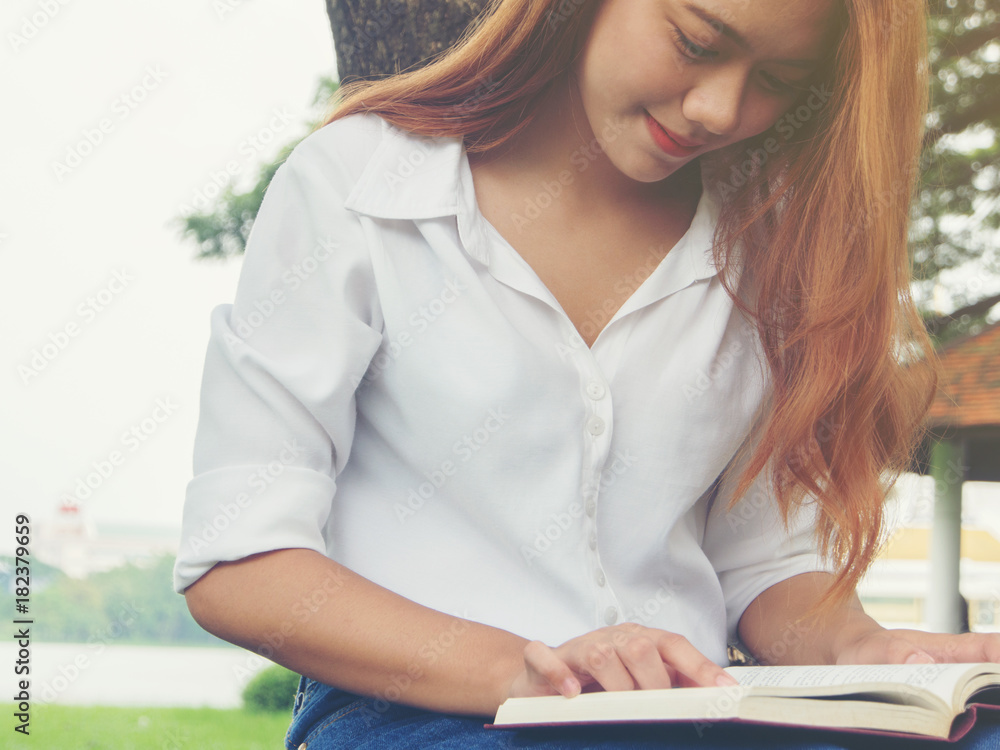Obraz premium Young woman sitting reading book at the park.