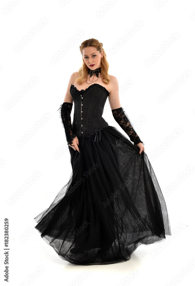 full length portrait of a blonde girl wearing black gothic gown. standing pose, isolated on white background.