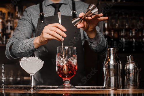 Barman making an alcoholic drink with ice in a cocktail glass