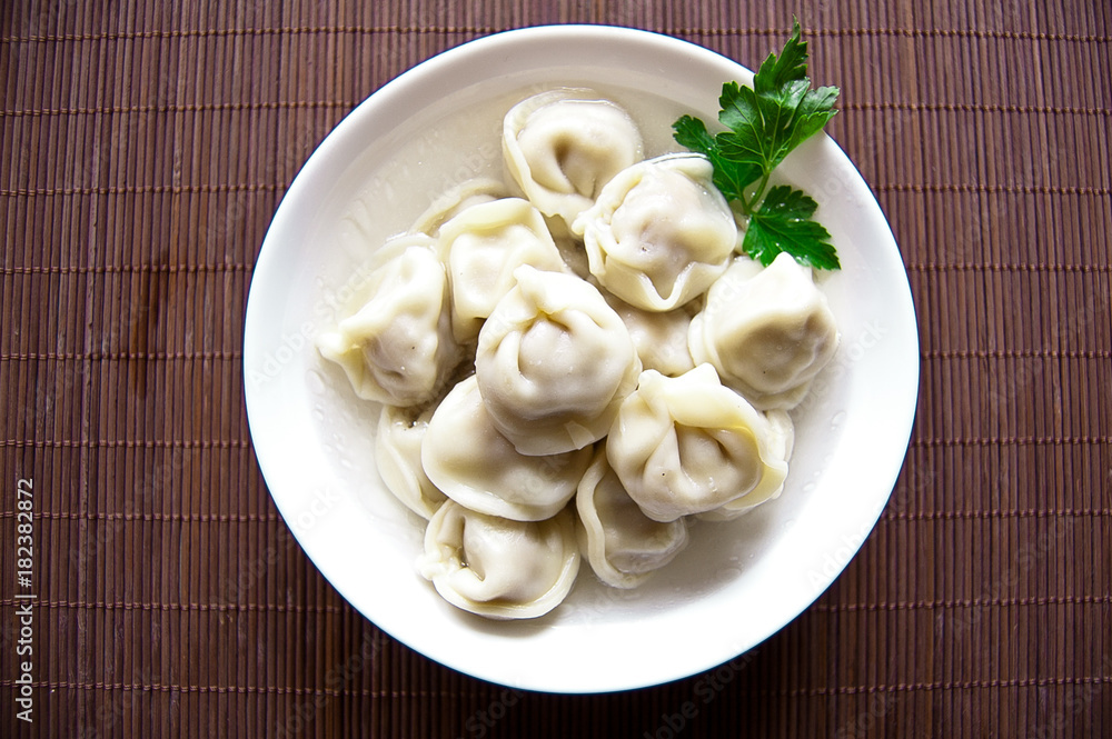 Home / purchased dumplings in a broth with greens. Dumplings are laid out in a deep white bowl. The bowl is on the stand. Day light. Dumplings are decorated with parsley leaves. Home / purchased dumplings in a broth with greens. Dumplings are laid out in a deep white bowl. The bowl is on the stand. Day light. Dumplings are decorated with parsley leaves.