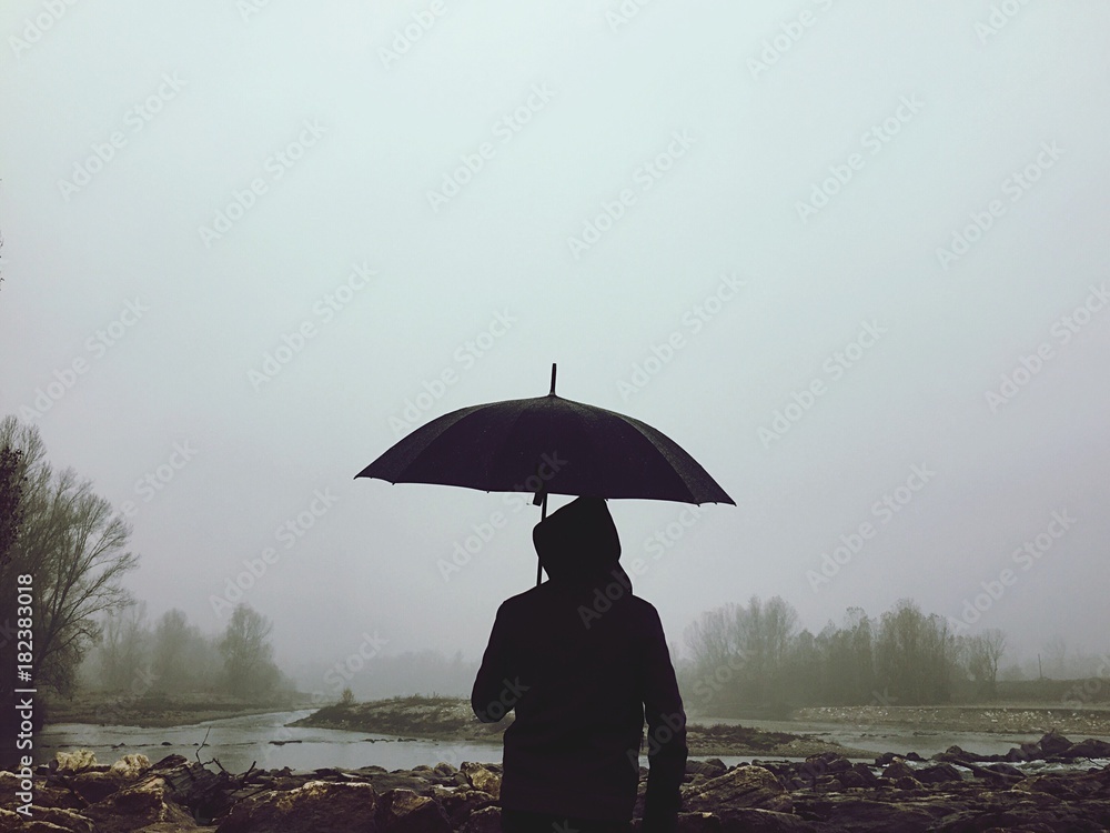 uomo con ombrello nella nebbia vicino al fiume