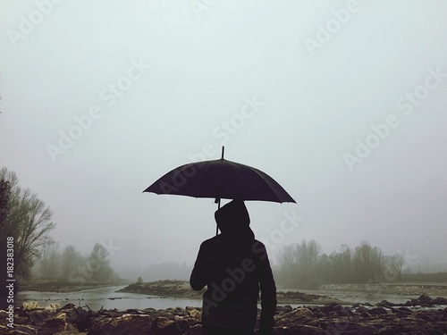 uomo con ombrello nella nebbia vicino al fiume photo