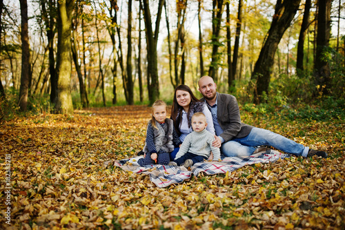 Happy caucasian family of mom dad and little girl with boy sitting on plaid at majestic autumn fall forest.