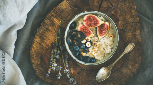 Healthy winter breakfast. Rice coconut porridge with figs, berries and hazelnuts in bowl over rustic wooden board background, top view. Clean eating, vegetarian, vegan, alkiline diet food concept