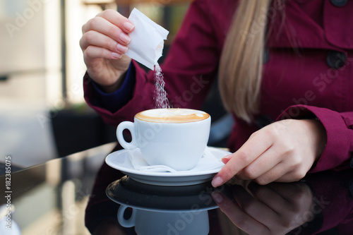 Young woman adding sugar to the coffee