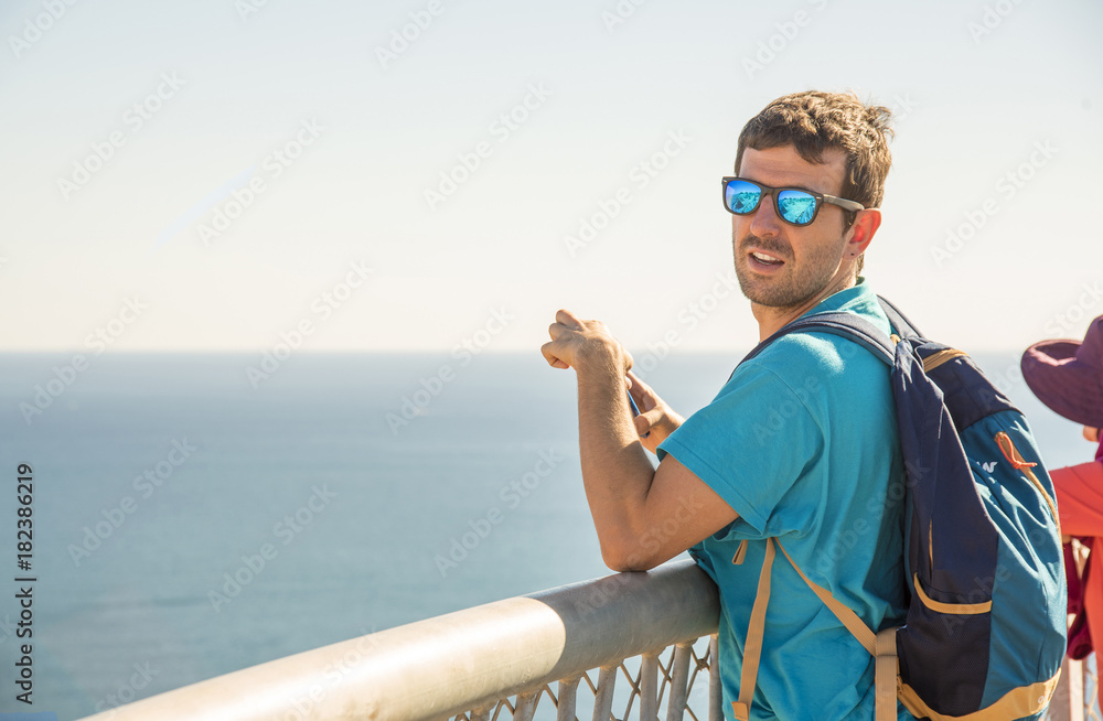 Joven sonriente con mobil en la mano apoyándose en el balcón del Mediterráneo  Con buen tioempo lo mejor es salir a la naturaleza y diverstirse