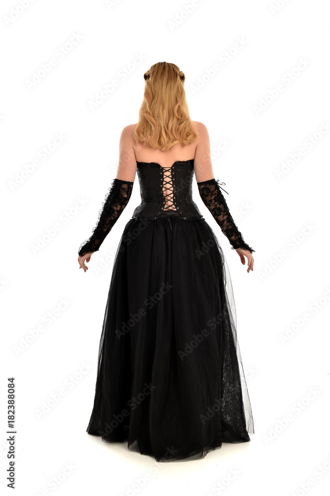 full length portrait of a blonde girl wearing black gothic gown. standing pose, isolated on white background.