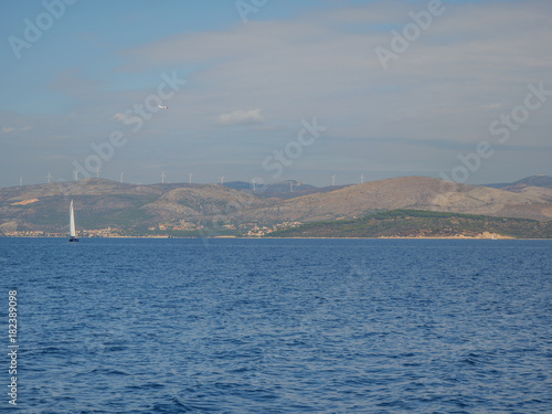 Croatian coastline with sailing boat and wind power generators on hills. © 2STOCKista