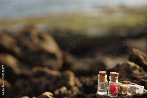 Small glass vessels with cork lids, filled with aromatic oil, salt and fragrant inflorescences on the rocks by the sea in the morning, spa set