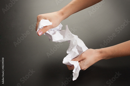 Female hands with paper on a black background. Studio. Tear, crumble the paper