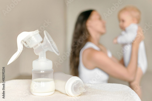 Manual breast pump and bottle with breast milk on the background of mother holding baby in her hands. Maternity and baby care.