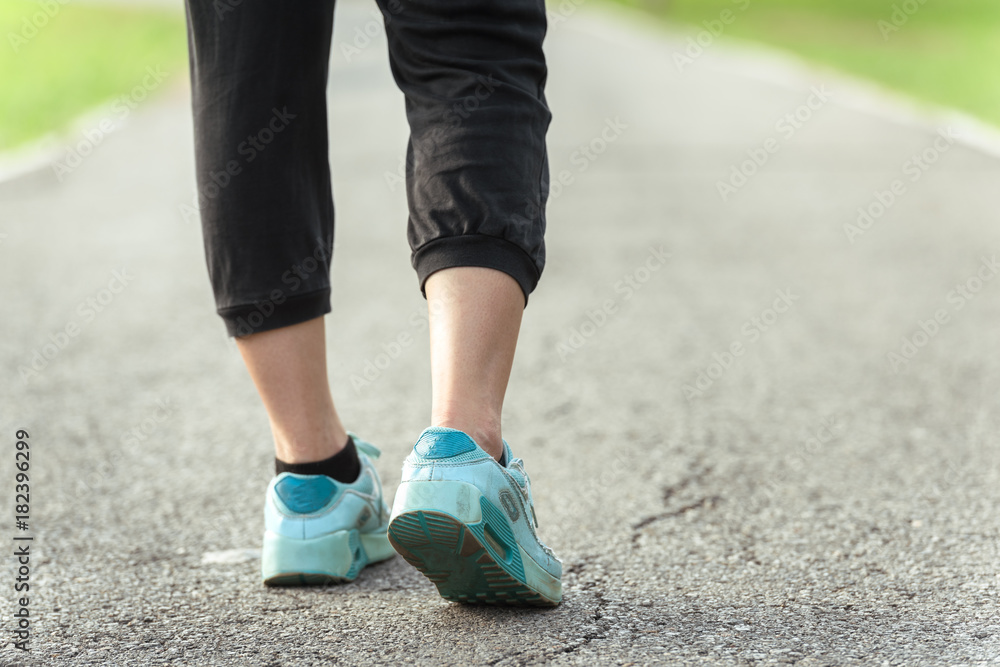 Runner feet running on asphalt road in park - fitness sunrise jogging workout wellness concept