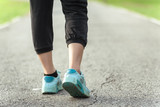 Runner feet running on asphalt road in park - fitness sunrise jogging workout wellness concept