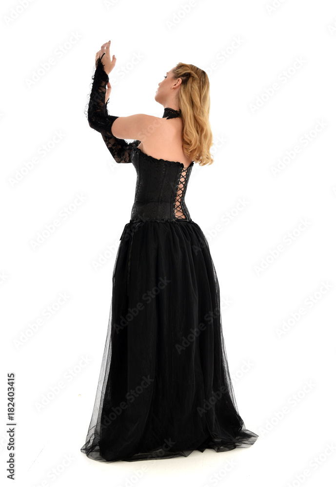 full length portrait of a blonde girl wearing black gothic gown. standing pose, isolated on white background.