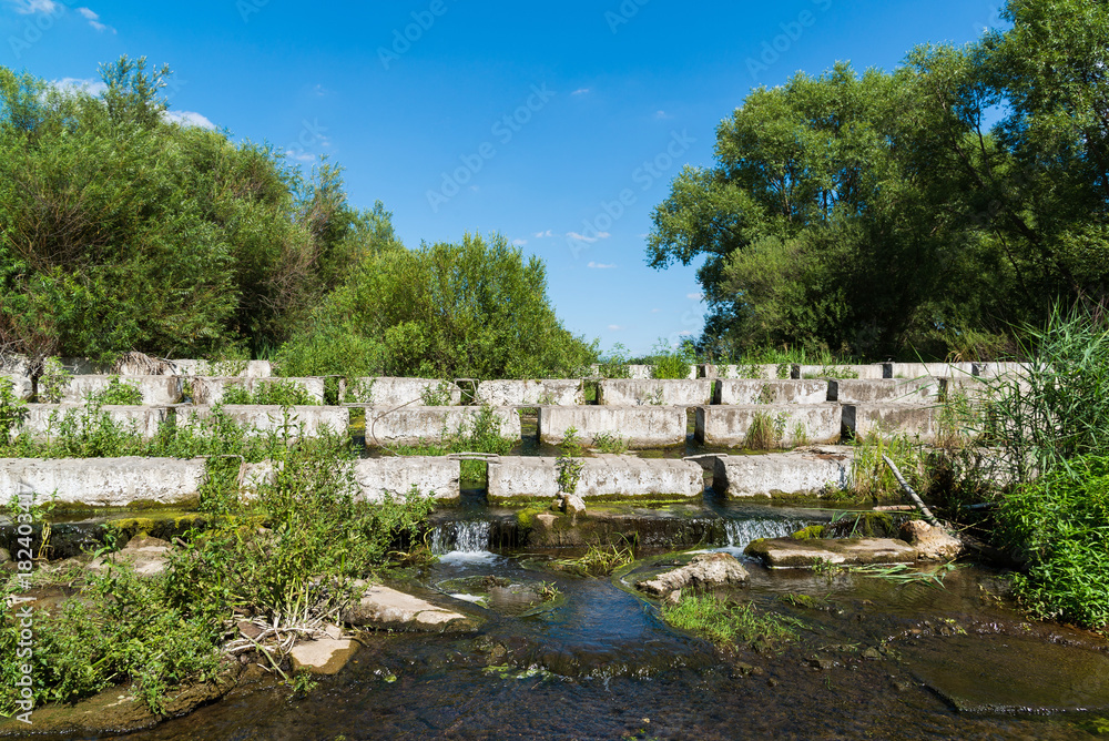 Fototapeta premium Concrete blocks lying on a small river - dam